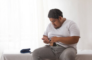 A fat fan trying to treat obesity with syringe by applying insulin injection to himself. - obrazy, fototapety, plakaty