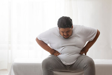  A fat man sitting and holding his belly in pain.