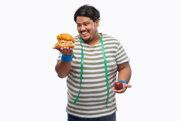 Portrait of a fat man with measuring tape around his neck greedily devouring  a burger rather than...