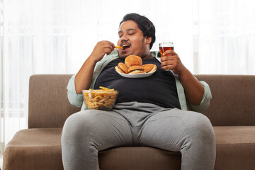  A fat man enjoying while sitting in his room eating junk food.