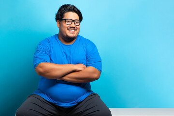 Portrait of a fat man wearing eyeglasses smiling while sitting cross armed. - obrazy, fototapety, plakaty