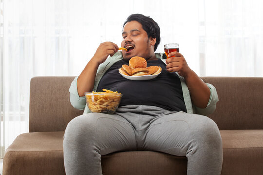  A fat man enjoying while sitting in his room eating junk food.