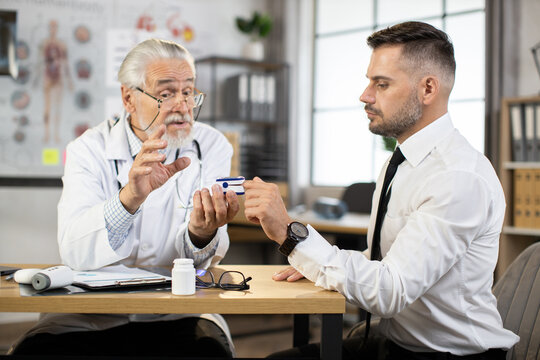 Competent senior doctor using finger pulse oximeter for testing oxygen level in blood of caucasian man in business wear. Concept of people, examination and treatment.