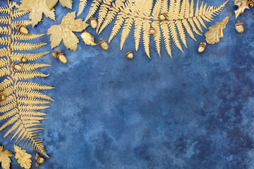 Gold leaf border with fern, sycamore, acorn and holly leaves with loose acorn nuts on mottled blue...