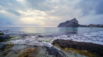 Panoramic landscape in the sea with a large mountain on the horizon and waves breaking against the rocks.