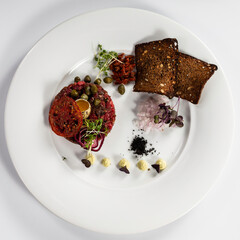 Beef tartare with yolk and bread toasts served on a white plate top view on white background.