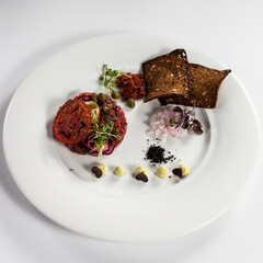 Beef tartare with yolk and bread toasts served on a white plate top view on white background.