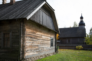 An old rustic wooden hut. In the background there is a rustic wooden church.