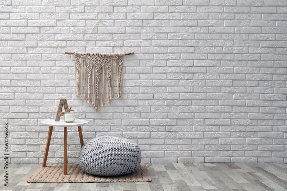 Sticker Comfortable knitted pouf, table and decor elements near white brick wall indoors, space for text. Interior design