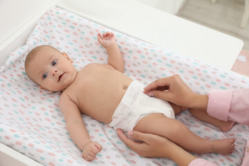 Mother changing her baby's diaper on table at home - obrazy, fototapety, plakaty