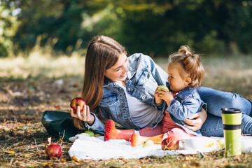 Young mother with her little daughter in an autumn park having picnic