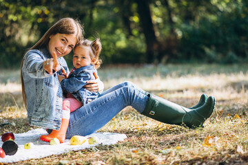 Fototapeta premium Young mother with her little daughter in an autumn park having picnic