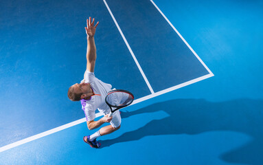 Full-length top view portrait of male professional tennis player serving a ball, training over gym...