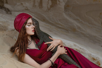 Portrait of a girl in a red turban hugs a monitor lizard