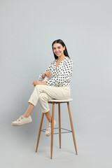 Beautiful young woman sitting on stool against light grey background