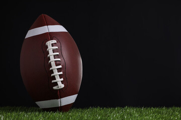 American football ball on green grass against black background. Space for text