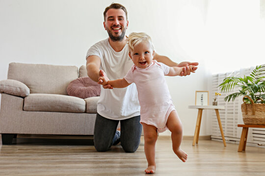 Father and daughter spending quality time together.A child learning to walk. Bearded man with his adorable blonde toddler. Close up, copy space for text, background.