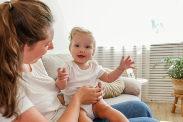 Portrait of a loving young mother holding her toddler child. Woman with her blonde child having fun at home. Close up, copy space for text, background.
