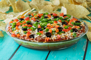 Close up of a freshly made Mexican layered dip, with chips in behind, ready for serving.