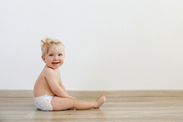 Portrait of one year old child sitting on the wooden floor over white wall background. Adorable...