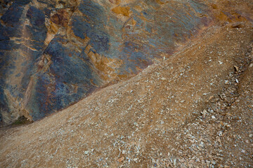 Fragment of multicolored rock and pieces of crushed rock along with sand, nature, landscape.