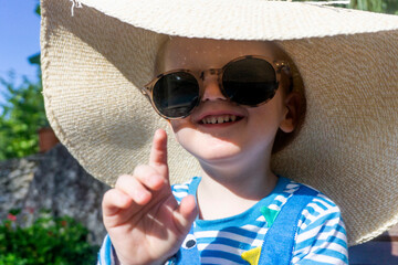 Cute little toddler wearing an oversized sun hat and sunglasses relaxing in the sun