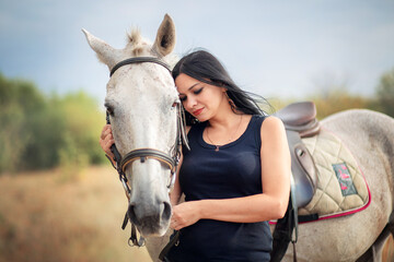 Fototapeta premium A beautiful young woman with black hair hugs a horse. Communication with animals