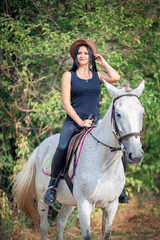 Beautiful woman in cowboy hat and leather pants rides a gray horse