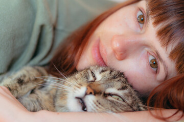 The woman lies with the cat in an embrace. Close-up.