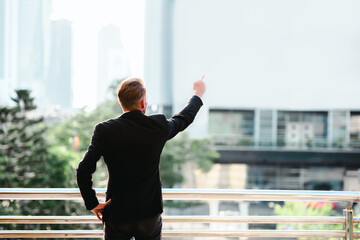 Vision concept, Successful businessman standing back and pointing finger away over white cityscape background. © sakarin14