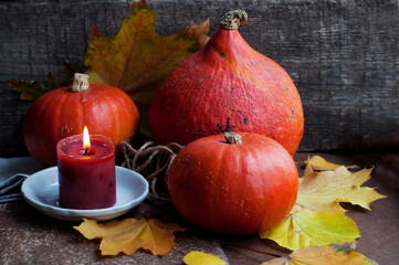 Pumpkins of different shapes with yellow autumn leaves and a candle on a wooden background