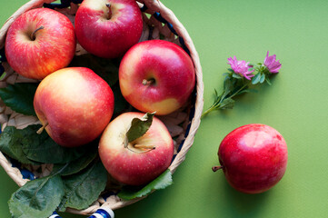 Fresh ripe red apples in a straw plate on a green background