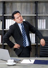 Asian businessman in a suit grab the waist with his hand. To alleviate pain from prolonged computer...