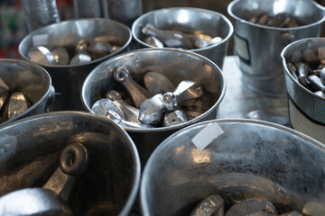 Hay diferentes piezas de plomo para la pesca en las cubetas de aluminio.