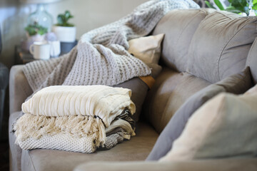 Stack of a variety of soft knit throw blankets stacked on a grey couch in a farmhouse style living room. Selective focus on covers with blurred foreground and background.
