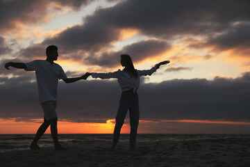 Happy couple dancing on beach at sunset