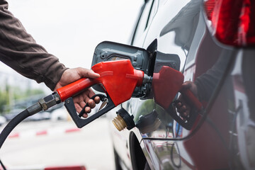 A gas station worker holds a fuel dispenser to fill the car with fuel. A young man's hand holds a...