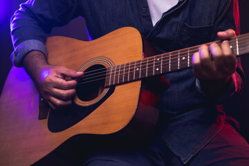 Close up hands young man playing acoustic guitar on stage live in concert. With neon light. Young man practicing music and solo guitar on the show.