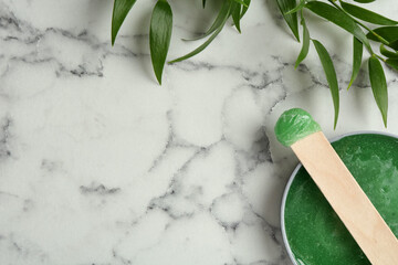 Spatula with wax and leaves on white marble table, flat lay. Space for text