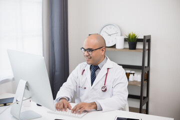 Young asian doctor working online texting on the keyboard video conference with team. Close Up Physician in white coat, stethoscope working with computer