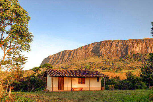 Small house, with the large stone wall of the Serra da Canastra massif in the background, at sunset, S&atilde;o Roque de Minas, Minas Gerais, Brazil
