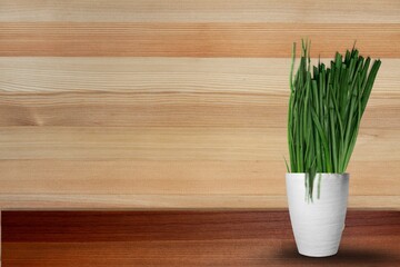 green onion in a white pot on the wooden background.