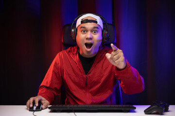 Excited and shocked face of Asian gamer with headphone playing computer pc video game online sitting at living room. Indian professional gamer streaming on social playing game very fun