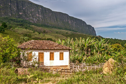Simple old farmhouse with corral, in the sunlight, with the large stone wall of the Serra da Canastra park massif in the background, S&atilde;o Roque de Minas, Minas Gerais, Brazil