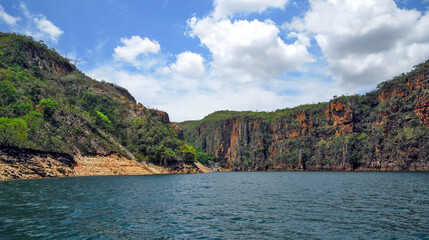 Fototapeta na wymiar Rocky walls, with vegetation on top, of the canyons of the huge lake of the Furnas dam, blue sky with clouds, Capitolio, Minas Gerais, Brazil