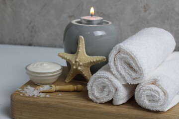 Fototapeta na wymiar salt for bath massage peeling spa relax massage. Home salon body care. Beauty. White towels starfish salt candles on a wooden tray on a gray background side view