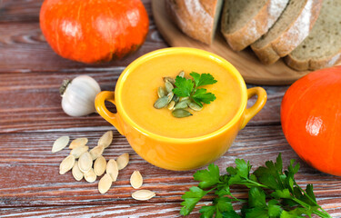 Pumpkin cream soup and freshly baked homemade bread on a wooden background. Close-up.