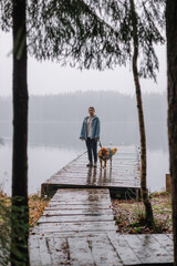 Attractive caucasian woman with brown Nova Scotia Duck Tolling Retriever walking on a wooden pier. Girl came for a walk with dog in the pine forest. Spending time with pets. Selective focus.
