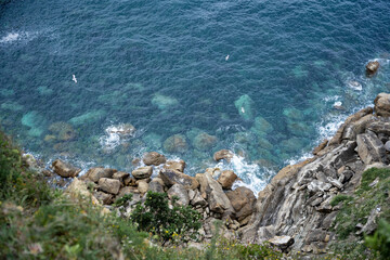 Top view from a cliff of blue sea with rocks and some seagulls