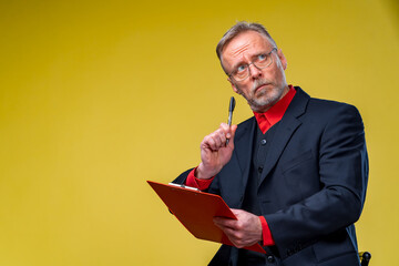 Portrait of a successful handsome businessman with red folder in hands. Mature man bites pen and looking away. Closeup